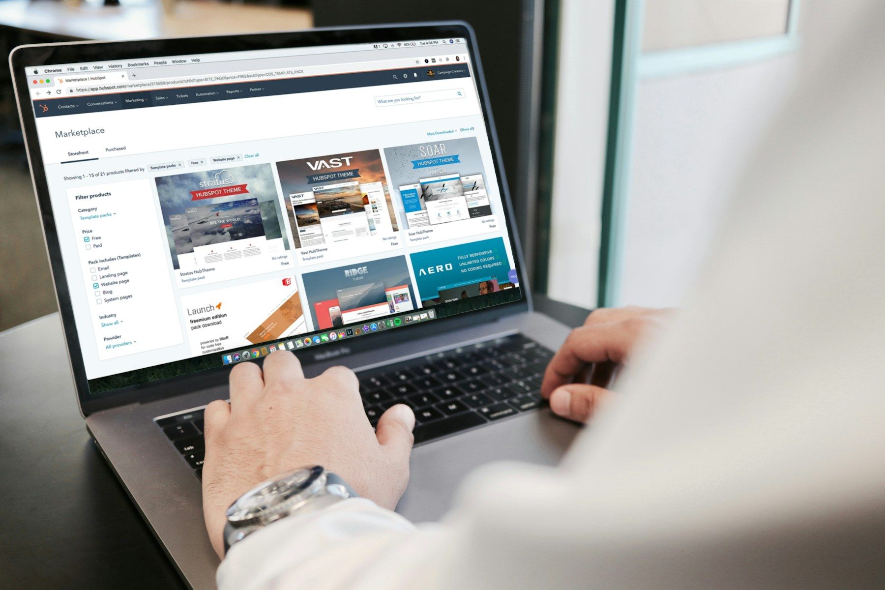 Hands on a laptop keyboard at an office desk, a website open on the screen