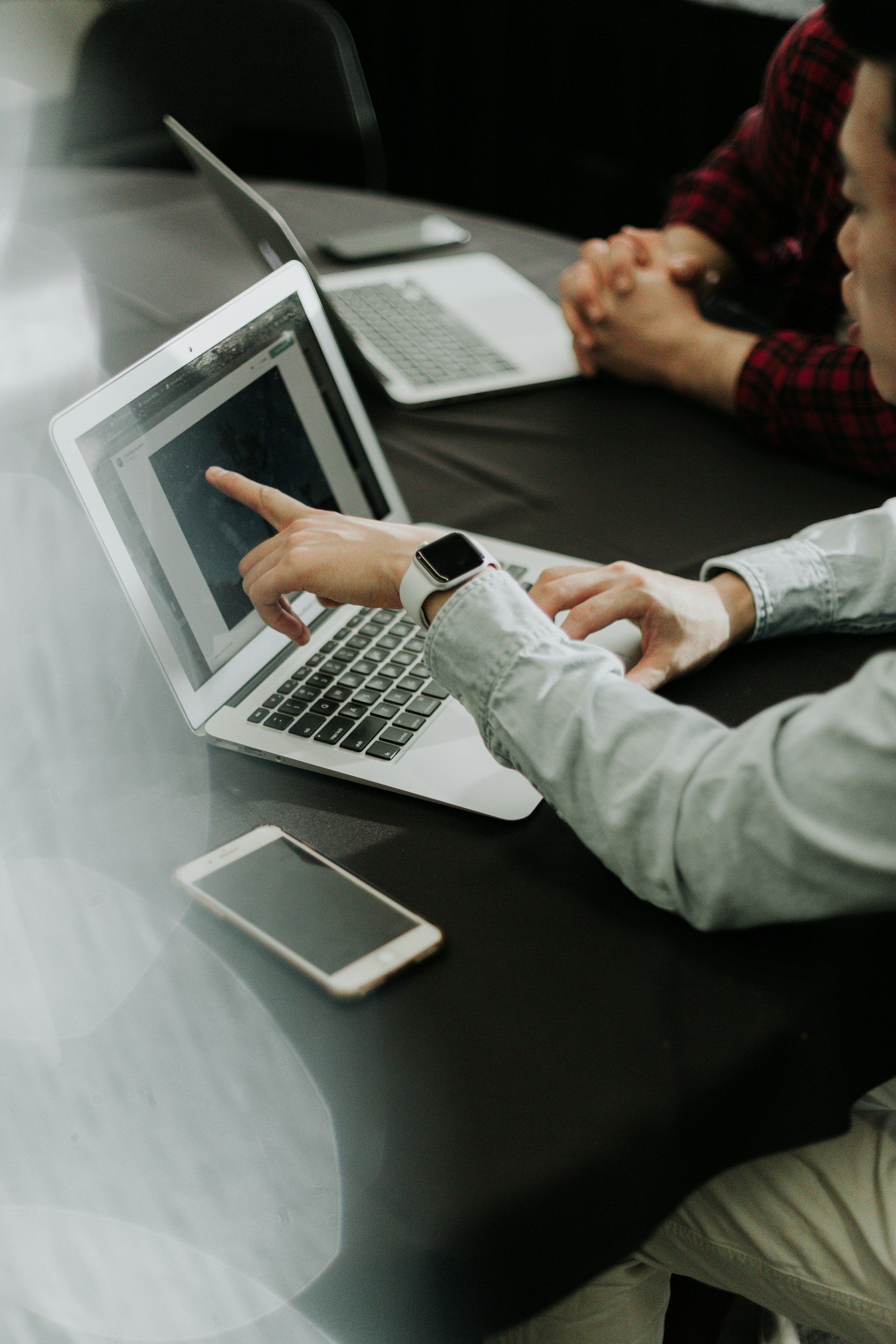 Two people at a meeting table, one pointing at a laptop screen while explaining a workflow